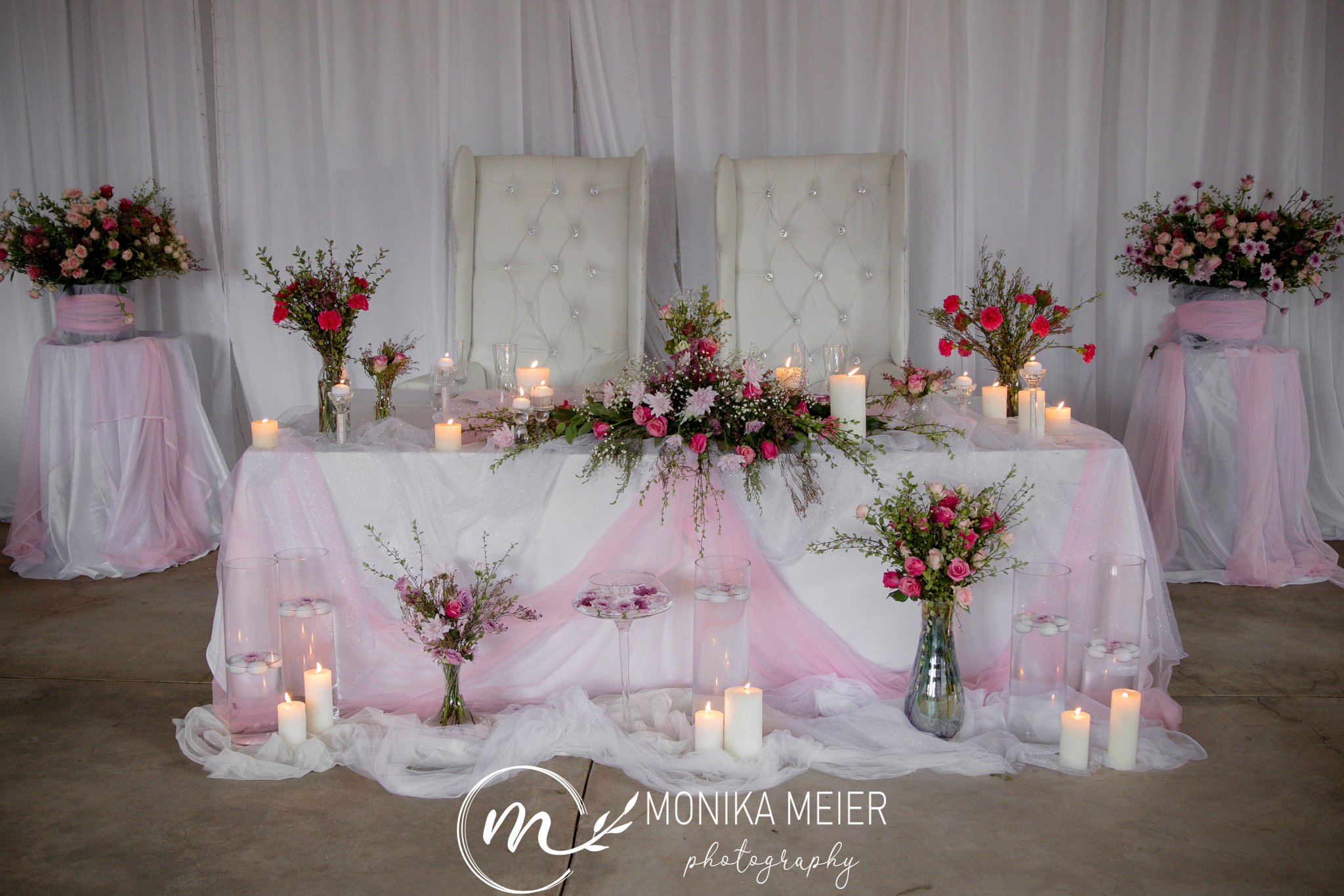 Pink and white wedding head table with flowers and candles.