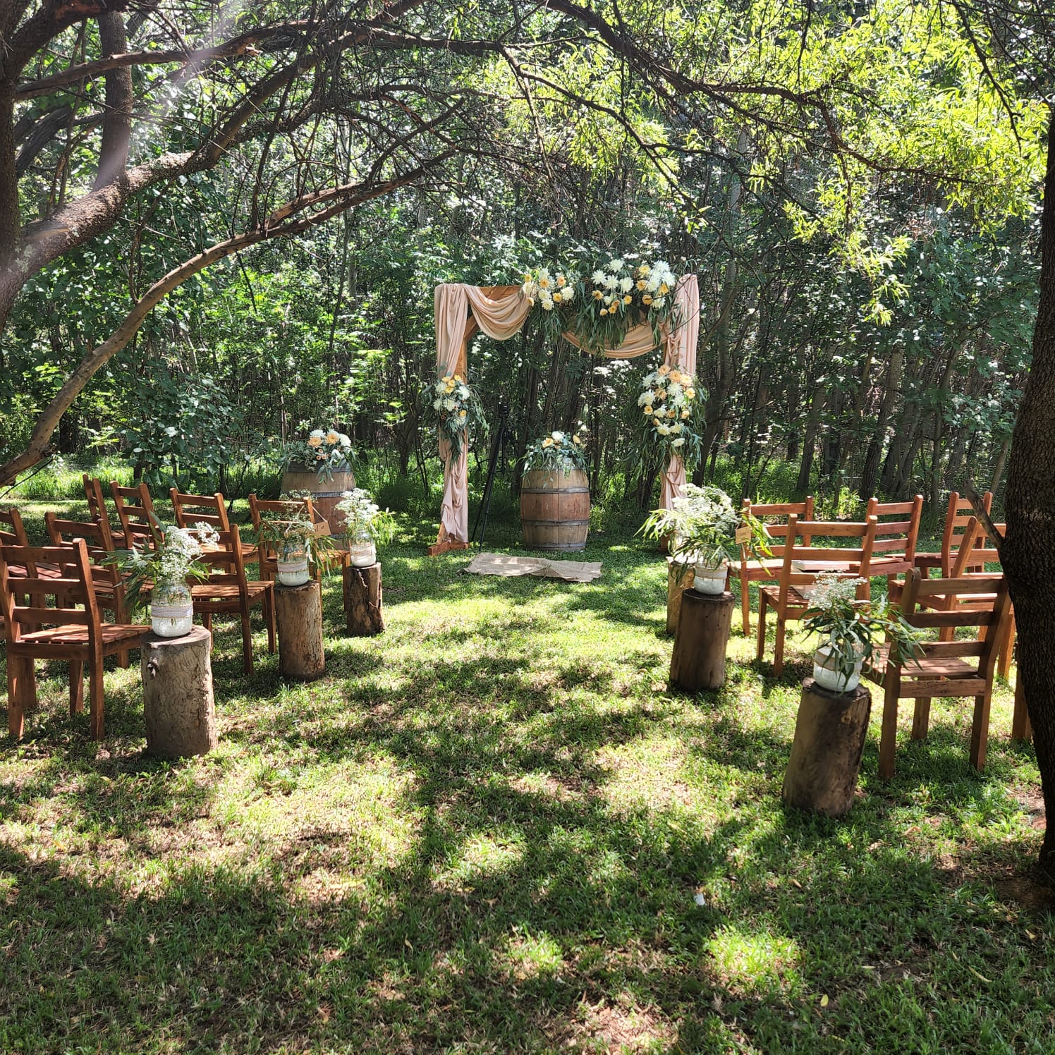 Outdoor ceremony seating with a peach draped floral arch.