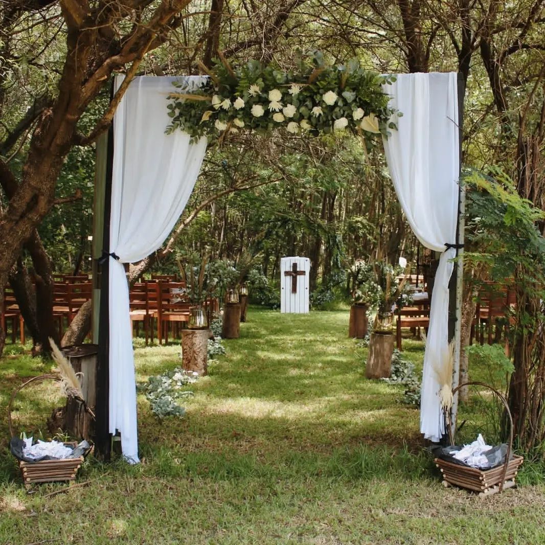 White draped floral arch and grassy wedding aisle beneath trees.