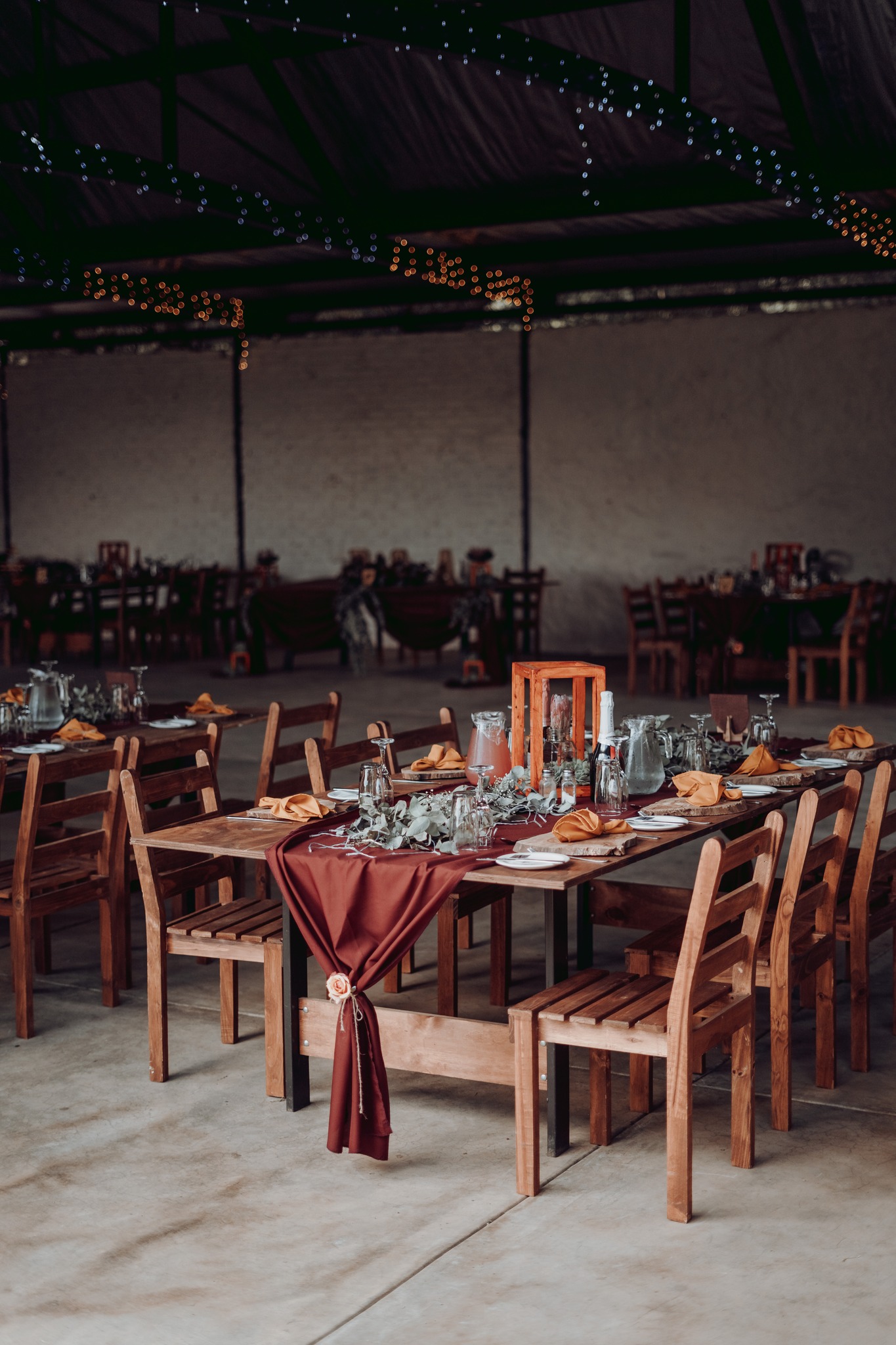 Rustic reception tables with warm burgundy runners and fairy lights.