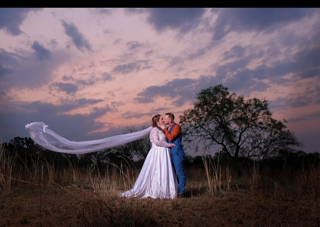 Wedding couple beneath a pink sunset sky with a flowing veil.